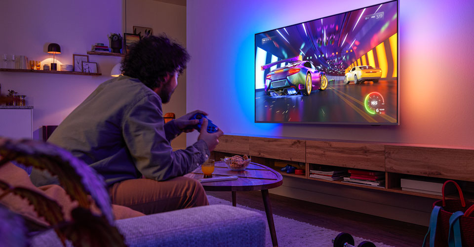 Bir kişi kanepede oturmuş, Philips Ambilight TV'de yarış video oyunu oynuyor