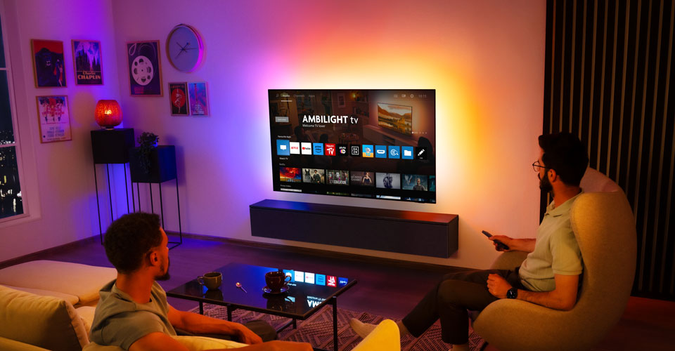 İki adam, oturma odasında duvara monte edilmiş bir Ambilight TV izliyor
